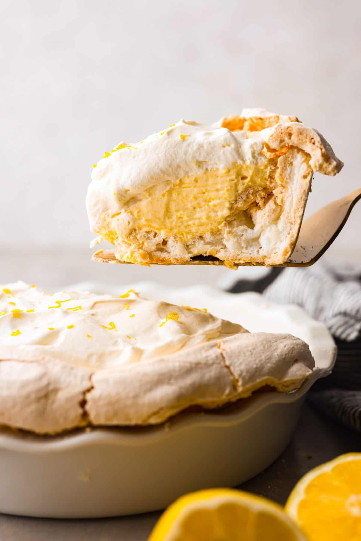 Lemon angel pie is a delightful dessert straight from heaven! It has a creamy lemon filling inside a sweet, airy meringue crust, then topped with fresh whipped cream. Every bite is pure bliss! Close view of a slice of lemon angle pie on a serving spatula.