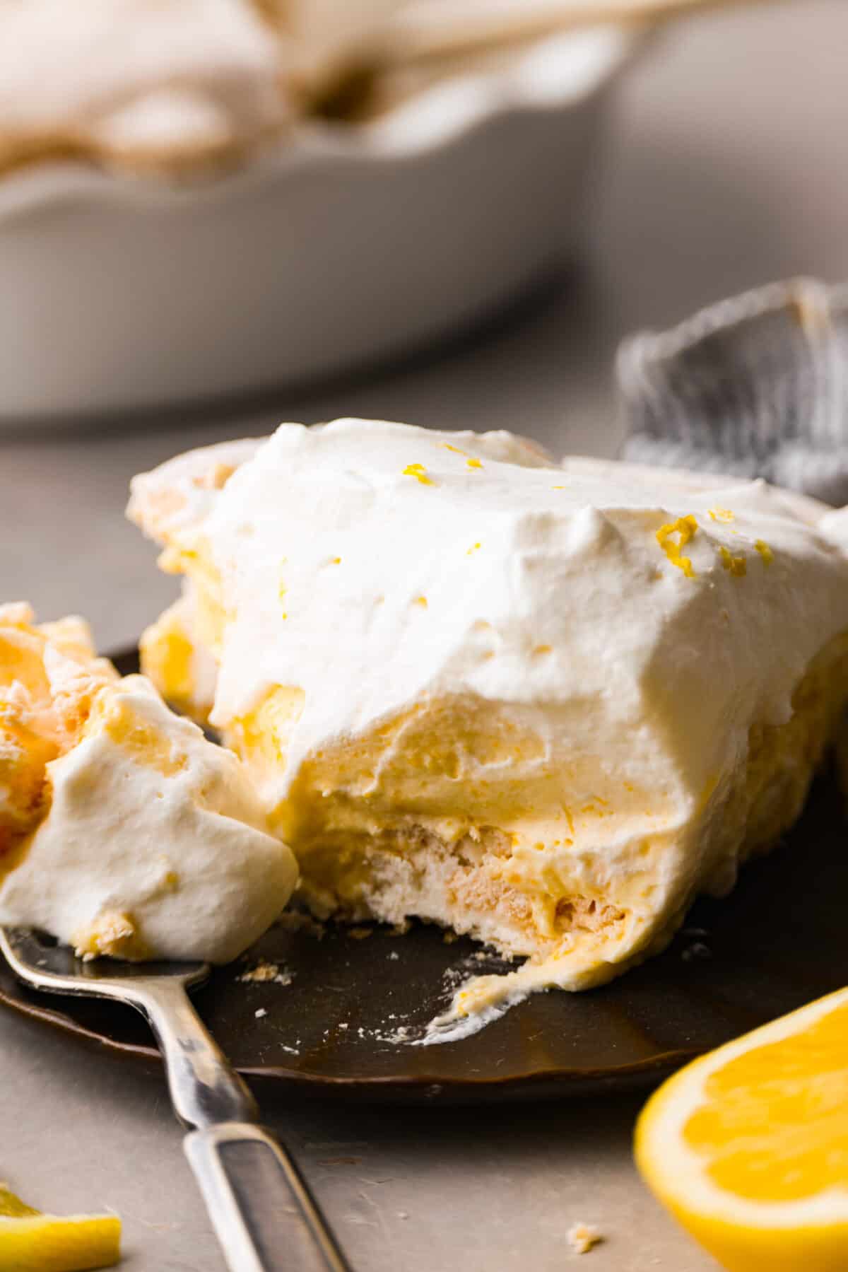Lemon angel pie is a delightful dessert straight from heaven! It has a creamy lemon filling inside a sweet, airy meringue crust, then topped with fresh whipped cream. Every bite is pure bliss! Close view of a slice of lemon pie on a plate with a fork.