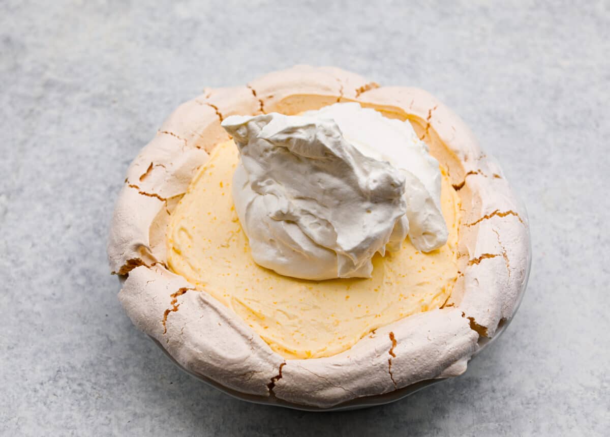 Lemon angel pie is a delightful dessert straight from heaven! It has a creamy lemon filling inside a sweet, airy meringue crust, then topped with fresh whipped cream. Every bite is pure bliss! Sixth process photo of the remaining whipped cream being spread on top of the lemon angel pie.