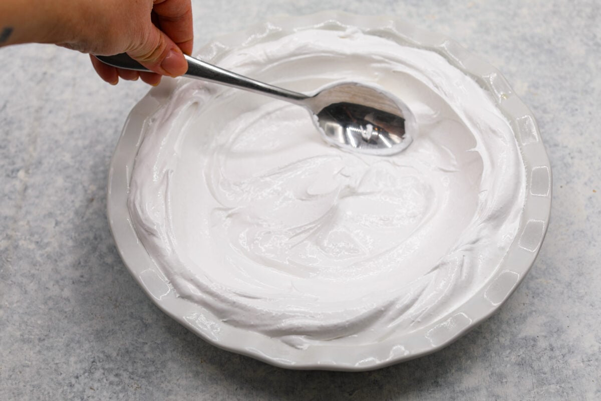 Lemon angel pie is a delightful dessert straight from heaven! It has a creamy lemon filling inside a sweet, airy meringue crust, then topped with fresh whipped cream. Every bite is pure bliss! Second process photo of the meringue spread inside the pie dish.
