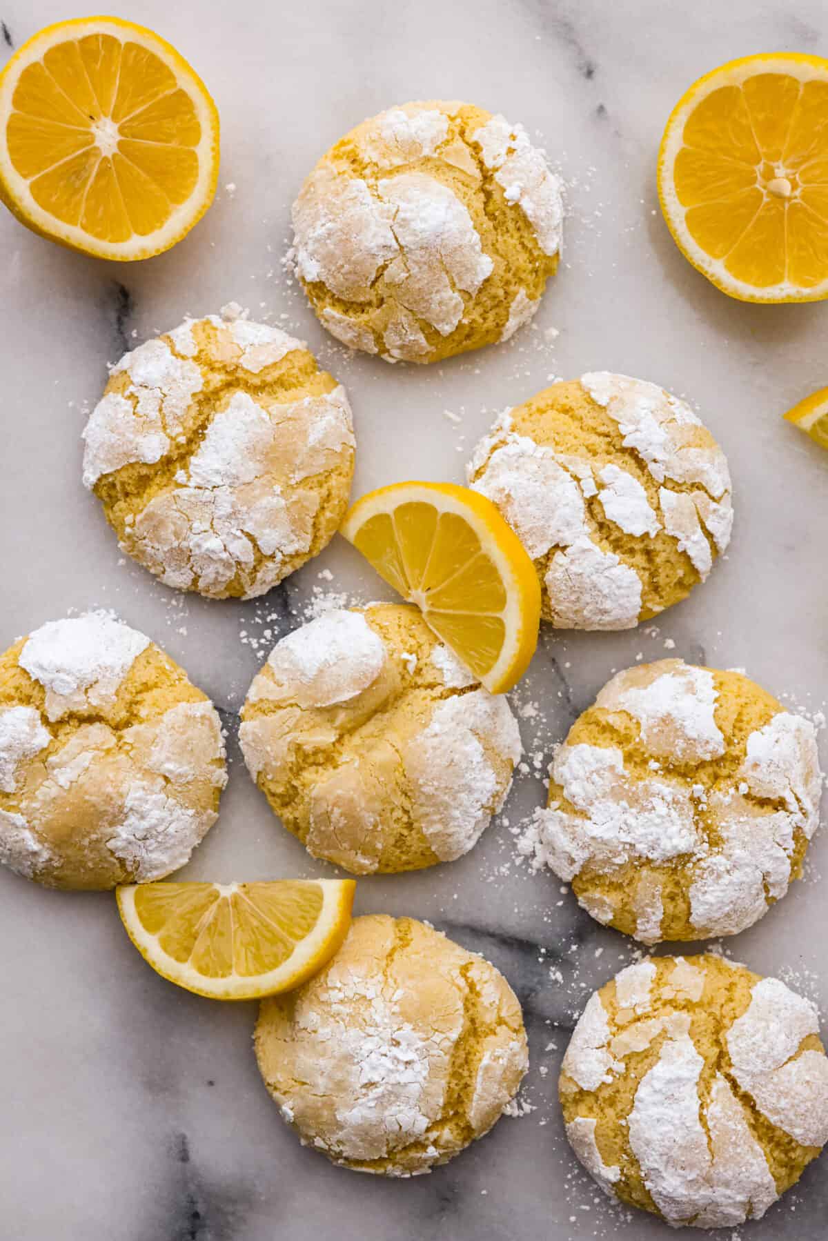 Lemon crinkle cookies are thick, soft pillows of lemon deliciousness! They have a refreshing flavor with an irresistible chewy texture. The perfect balance of sweet and tart make these a welcome treat for any occasion! Top-down view of the lemon crinkle cookies, garnished with lemon slices