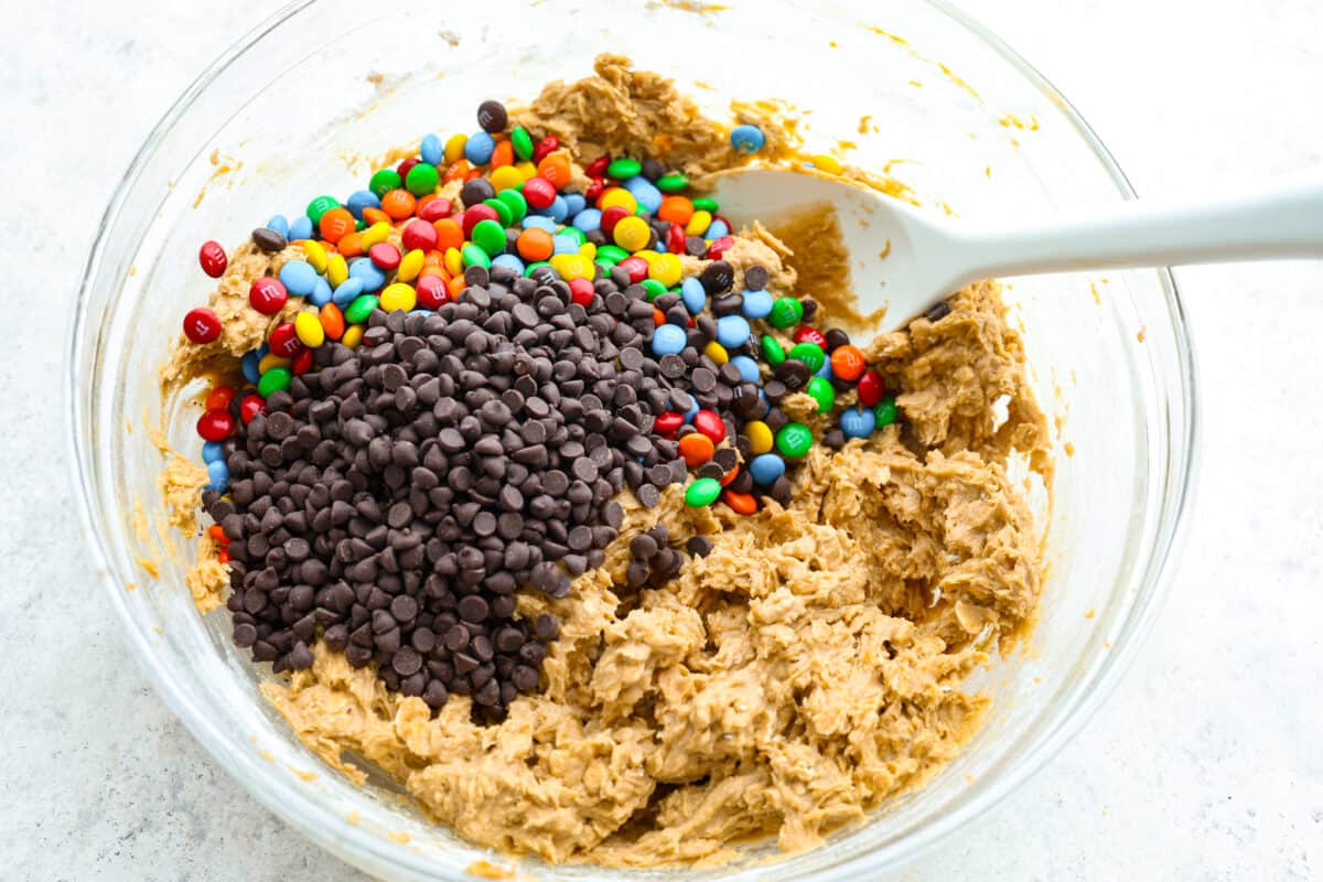 Monster cookies are slightly crisp on the outside, and soft and chewy in the center. They are loaded with peanut butter, oats, M&M candies, AND chocolate chips! Big monster cookies win every time! Process photo of cookie dough mixed with M&M's and chocolate chips added to the bowl.