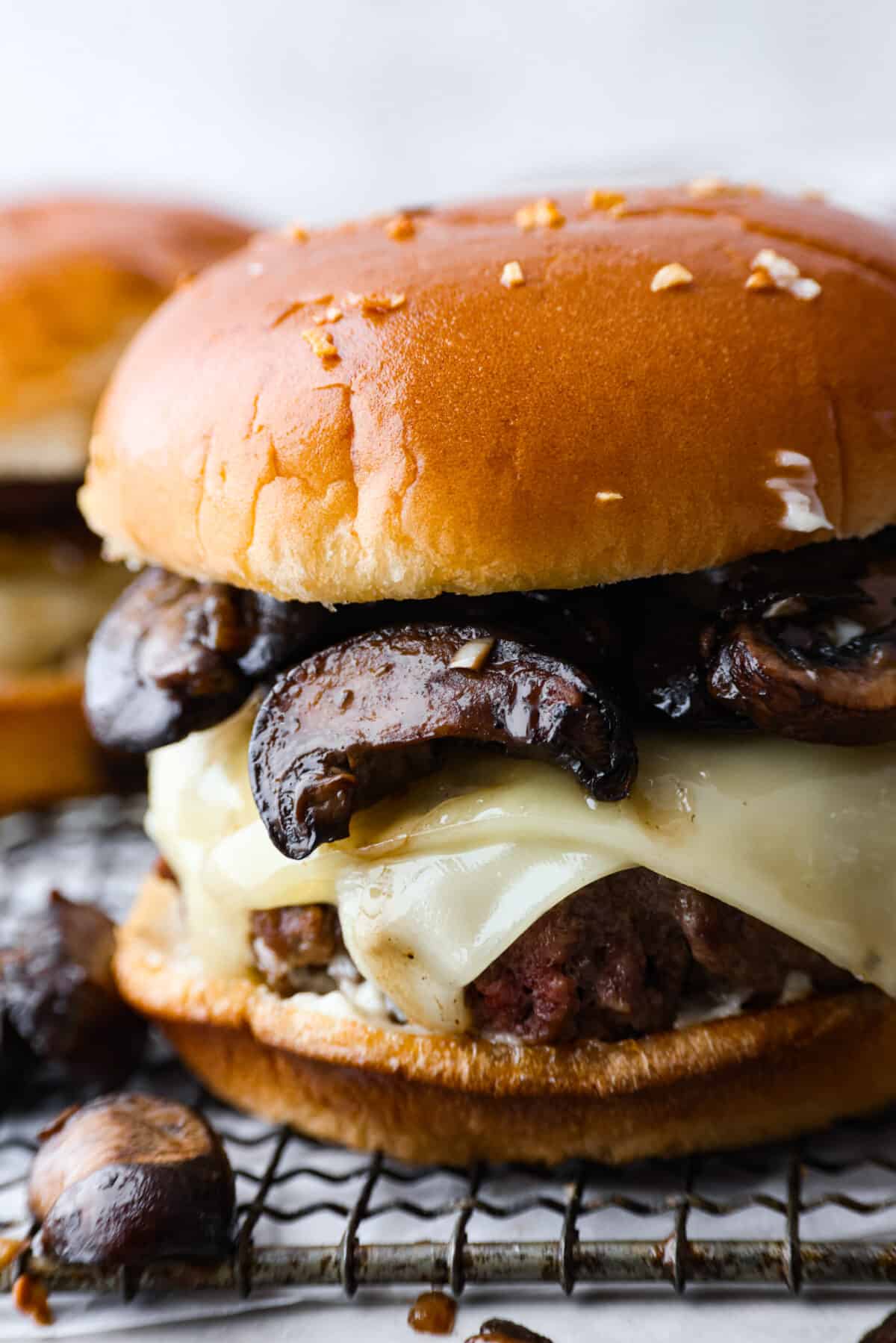 Create the most flavorful, juicy Mushroom Swiss Burger! Perfectly seasoned ground beef is topped with sautรฉed buttery mushrooms and melty Swiss cheese then loaded on fluffy buns for a gourmet burger that's easy to make at home! A closeup of a mushroom Swiss burger.