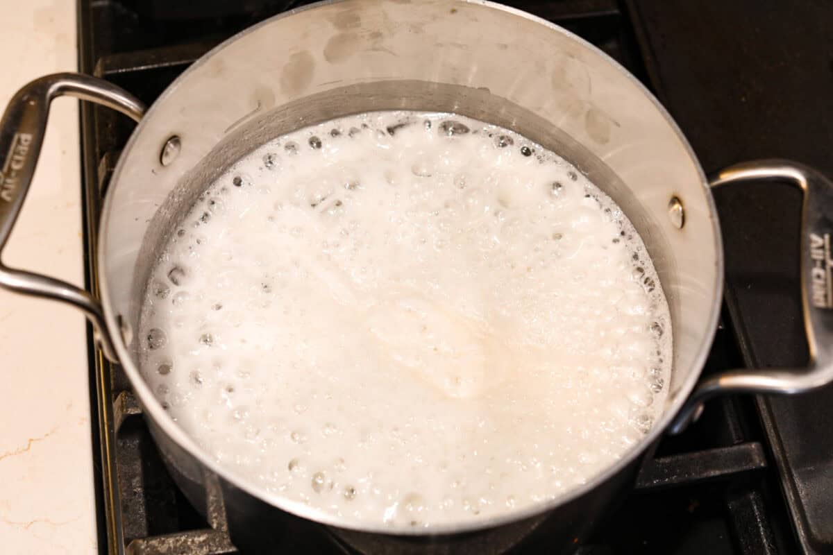 Treat yourself to this luxurious and refreshing Swedish Cream, a classic dessert that's easy to make. With a few simple ingredients and some chill time, you'll have a delightful treat topped with fresh berries and mint. Overhead shot of silver put with mixture boiling and foaming on the stovetop.