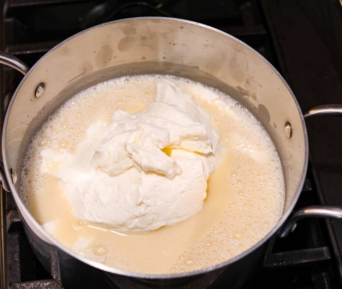 Treat yourself to this luxurious and refreshing Swedish Cream, a classic dessert that's easy to make. With a few simple ingredients and some chill time, you'll have a delightful treat topped with fresh berries and mint. Overhead shot of silver pot with boiled mixture with pile of sour cream in the middle.