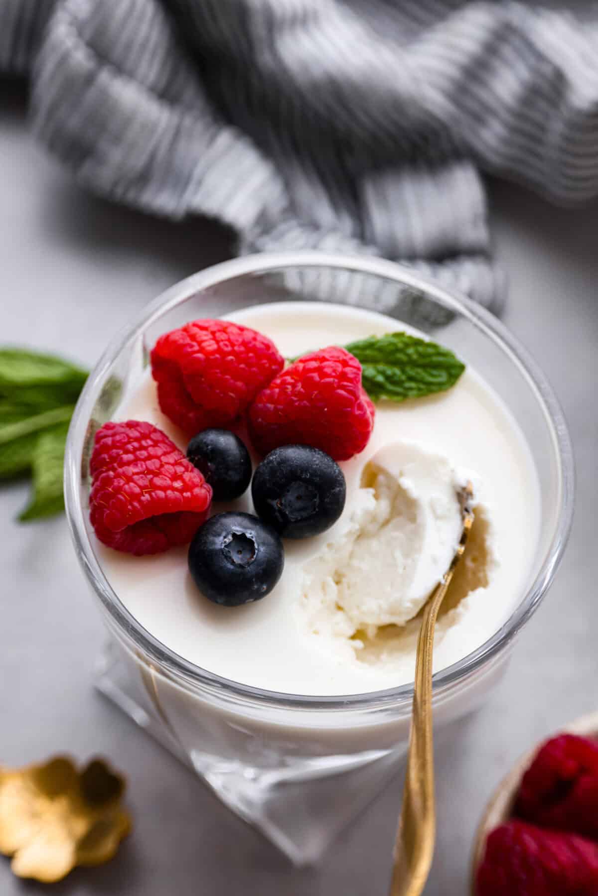 Treat yourself to this luxurious and refreshing Swedish Cream, a classic dessert that's easy to make. With a few simple ingredients and some chill time, you'll have a delightful treat topped with fresh berries and mint. Close up shot of the top of an individual cup of Swedish cream with berries and mint on top, with a gold spoon scooping a bite out of it.
