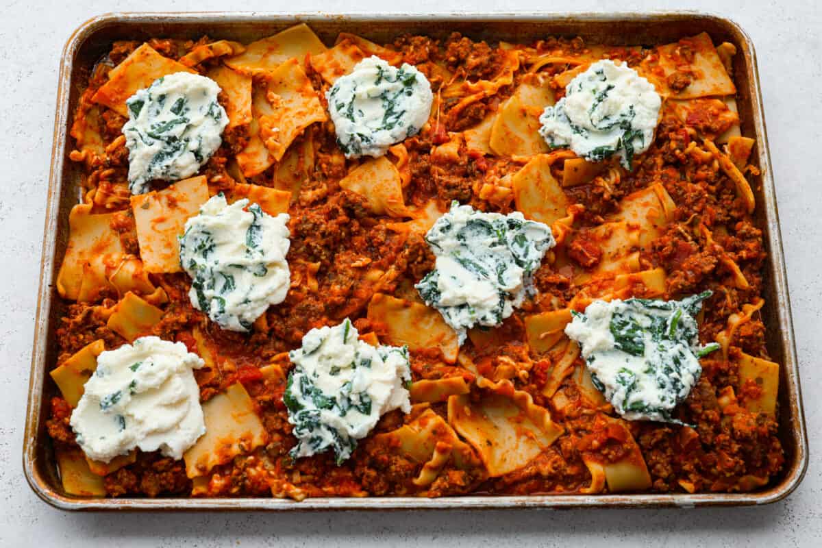 This super easy sheet pan lasagna is stacked with sautรฉedย ground beef and Italianย sausage that are cooked together, marinaraย sauce,ย creamy spinach ricotta, lasagna noodles and melty cheese for an amazingย Italian dinner. Dollops of spinach and ricotta on top of the noodles.