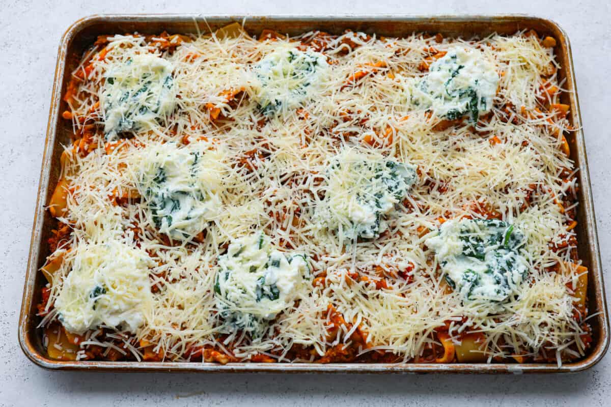 This super easy sheet pan lasagna is stacked with sautรฉedย ground beef and Italianย sausage that are cooked together, marinaraย sauce,ย creamy spinach ricotta, lasagna noodles and melty cheese for an amazingย Italian dinner. Shredded cheese sprinkled on top of sheet pan lasagna.