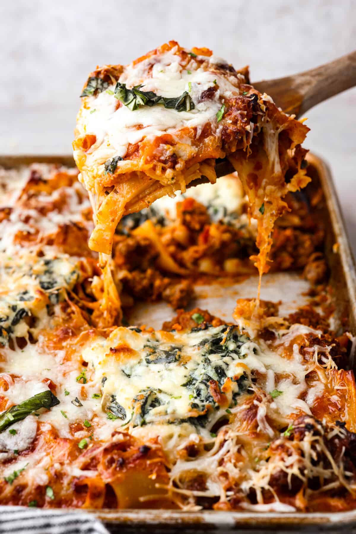 This super easy sheet pan lasagna is stacked with sautรฉedย ground beef and Italianย sausage that are cooked together, marinaraย sauce,ย creamy spinach ricotta, lasagna noodles and melty cheese for an amazingย Italian dinner. Sheet pan lasagna being served out of a sheet pan with a wooden spoon.