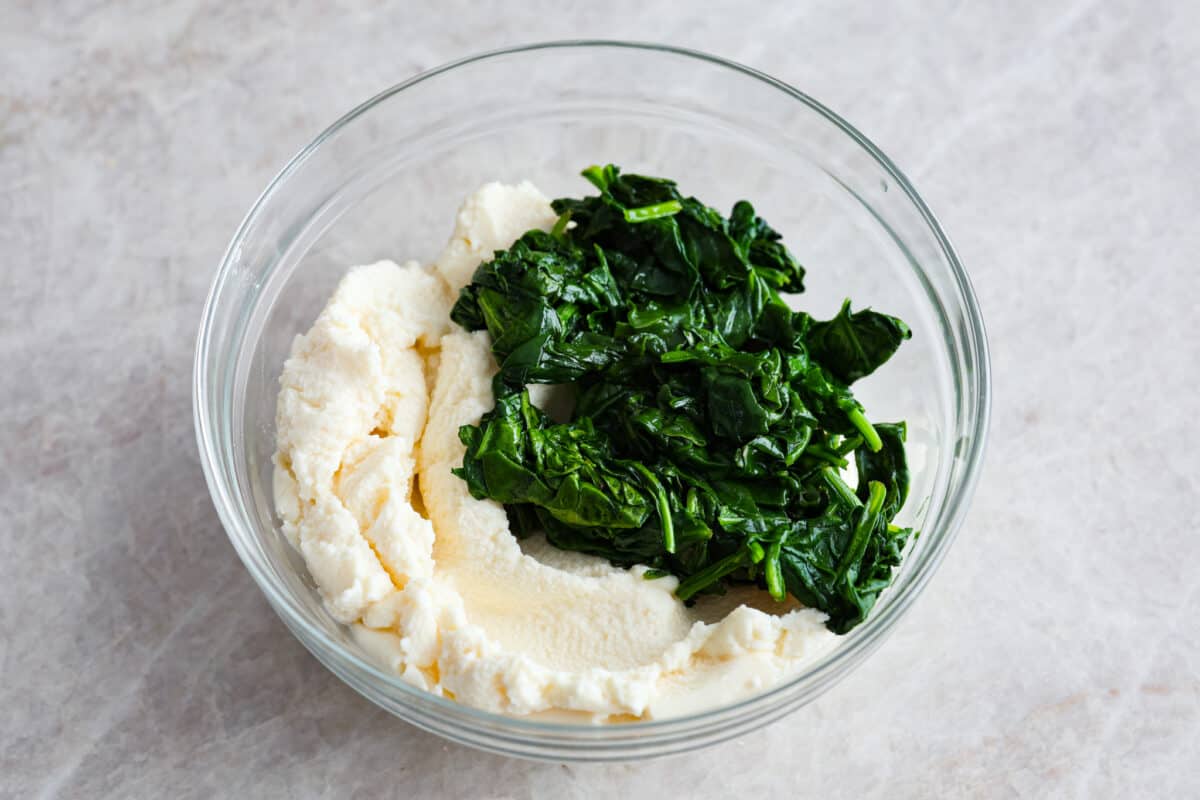 This super easy sheet pan lasagna is stacked with sautรฉedย ground beef and Italianย sausage that are cooked together, marinaraย sauce,ย creamy spinach ricotta, lasagna noodles and melty cheese for an amazingย Italian dinner. Cooked spinach and ricotta in a glass bowl.