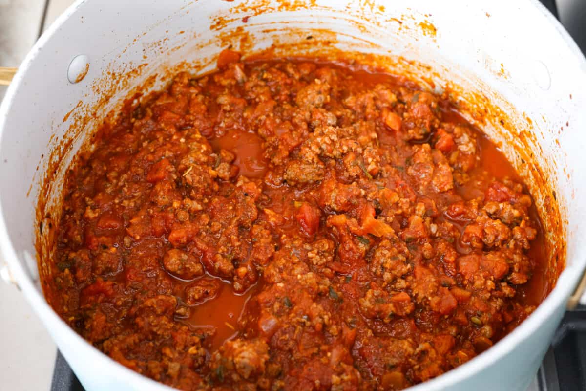 This super easy sheet pan lasagna is stacked with sautรฉedย ground beef and Italianย sausage that are cooked together, marinaraย sauce,ย creamy spinach ricotta, lasagna noodles and melty cheese for an amazingย Italian dinner. Marinara meat sauce simmering in a white pot being prepared to add to the sheet pan lasagna.