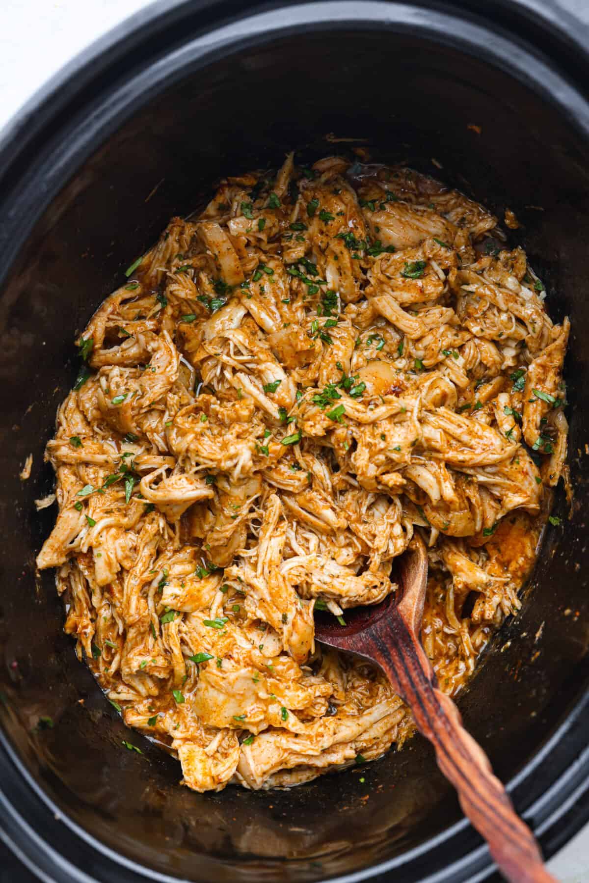 Switch up taco night with these 4-ingredient slow cooker ranch tacos! The chicken shreds perfectly and is packed with flavor. Dinner has never been easier! Top view of cooked in a slow cooker with a wooden spoon and cilantro garnished on top.