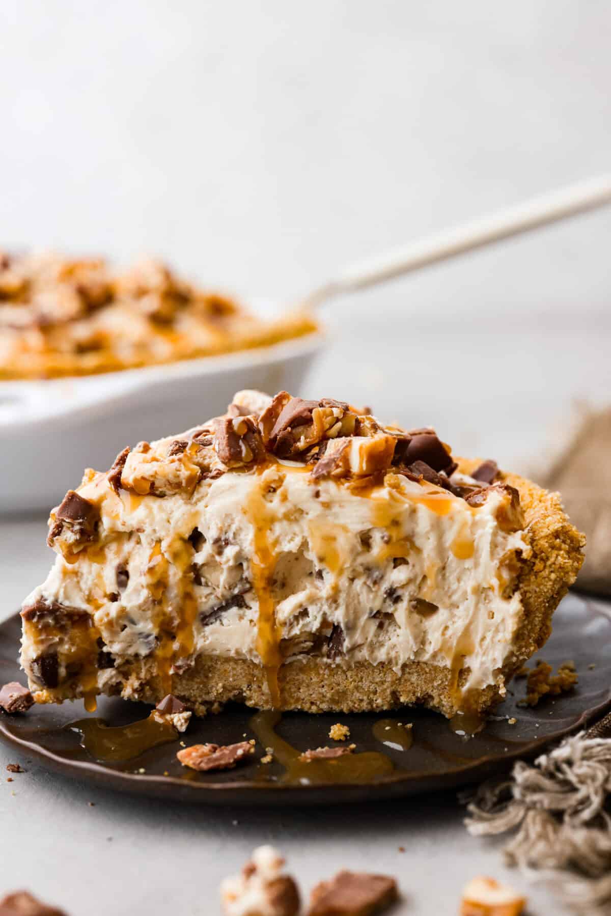 No Bake Snickers Bar Pie is one of the easiest and most delicious no bake pies that you make. You will love the Snickers pieces in every bite! A slice of no bake snicker bar pie on a black plate.