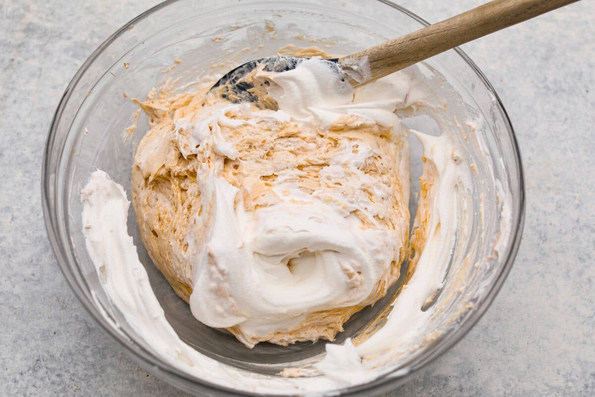 No Bake Snickers Bar Pie is one of the easiest and most delicious no bake pies that you make. You will love the Snickers pieces in every bite! Whipped Topping being added into the bowl of ingredients.