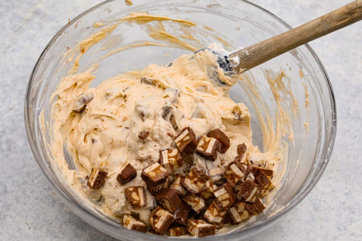 No Bake Snickers Bar Pie is one of the easiest and most delicious no bake pies that you make. You will love the Snickers pieces in every bite! Chopped snickers bar being added into the glass bowl of filling for the no bake snickers bar pie.