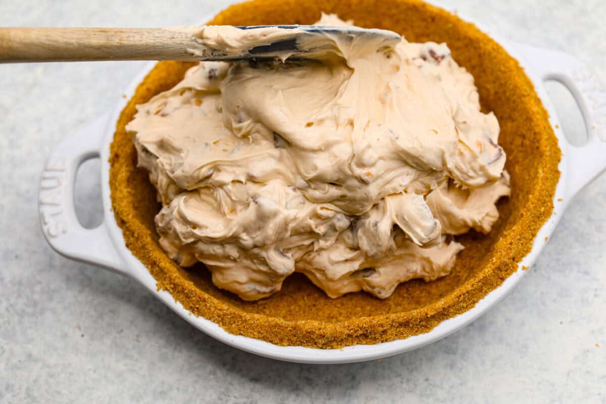 No Bake Snickers Bar Pie is one of the easiest and most delicious no bake pies that you make. You will love the Snickers pieces in every bite! Filling for the no bake snickers bar pie being added to the pie crust.