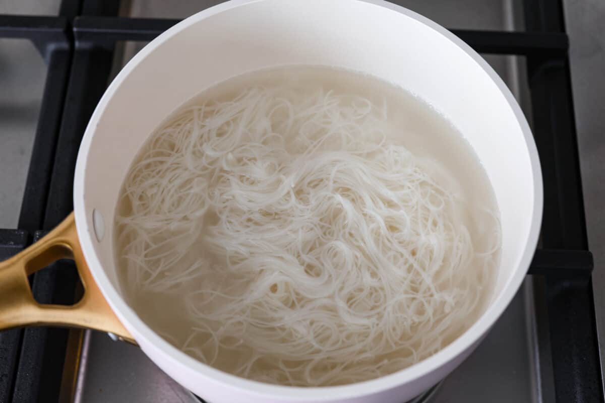Spring rolls are a delightful, fresh, and vibrant snack that's perfect for any occasion. With ingredients like crisp carrots, refreshing mint, and tender rice vermicelli, these rolls are not only healthy but also bursting with flavor. Noodles in a pot in water on the stove.