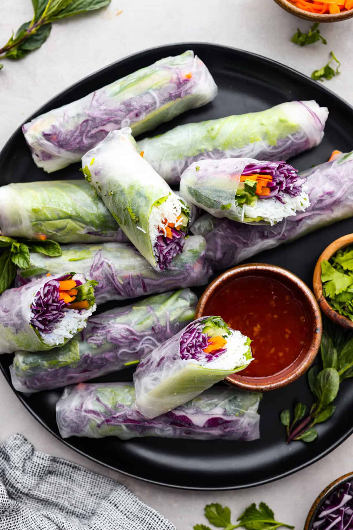Spring rolls are a delightful, fresh, and vibrant snack that's perfect for any occasion. With ingredients like crisp carrots, refreshing mint, and tender rice vermicelli, these rolls are not only healthy but also bursting with flavor. Spring rolls on a plate with chili dipping sauce.