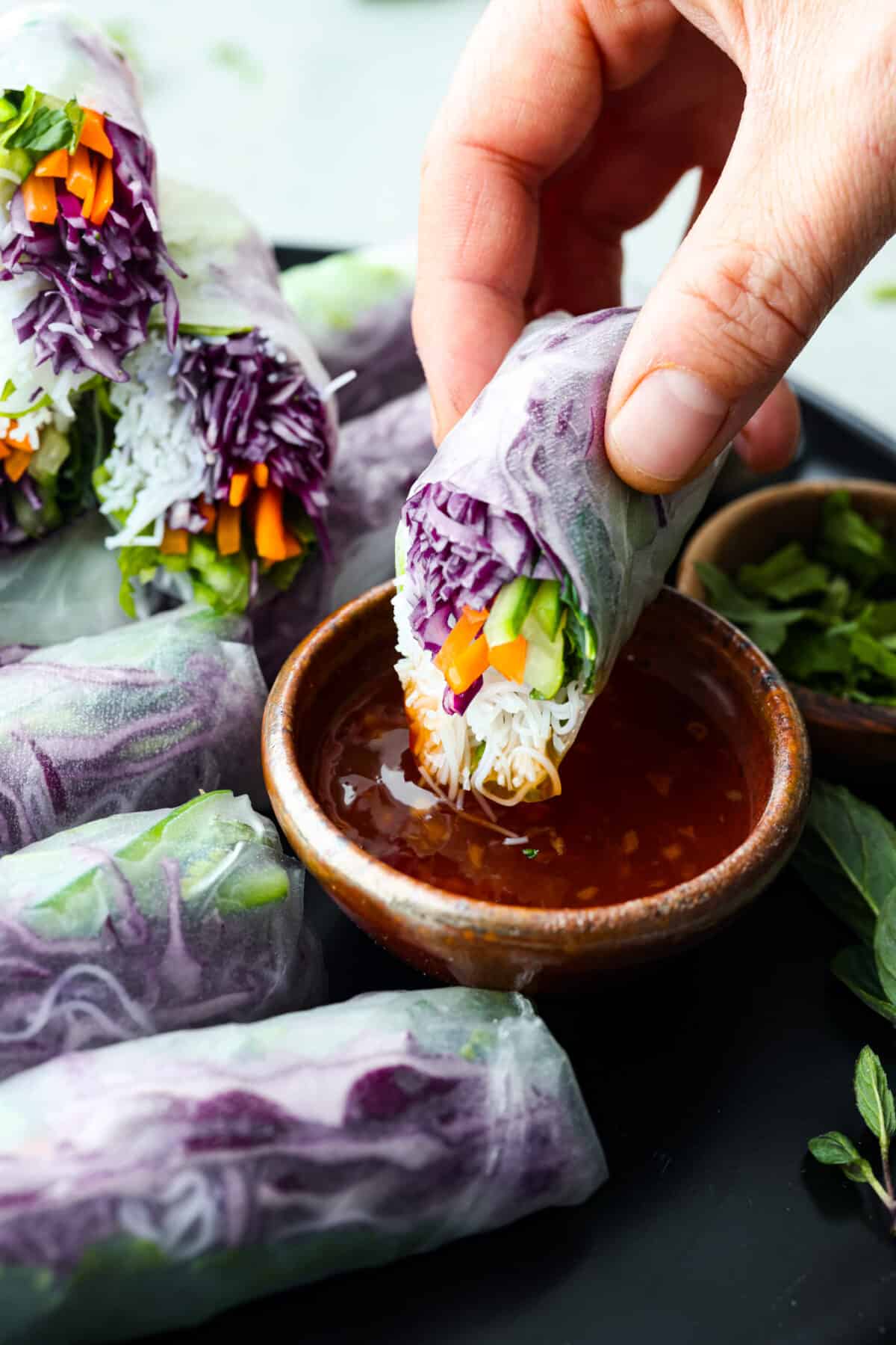 Spring rolls are a delightful, fresh, and vibrant snack that's perfect for any occasion. With ingredients like crisp carrots, refreshing mint, and tender rice vermicelli, these rolls are not only healthy but also bursting with flavor. A spring roll being dipped into cili sauce.
