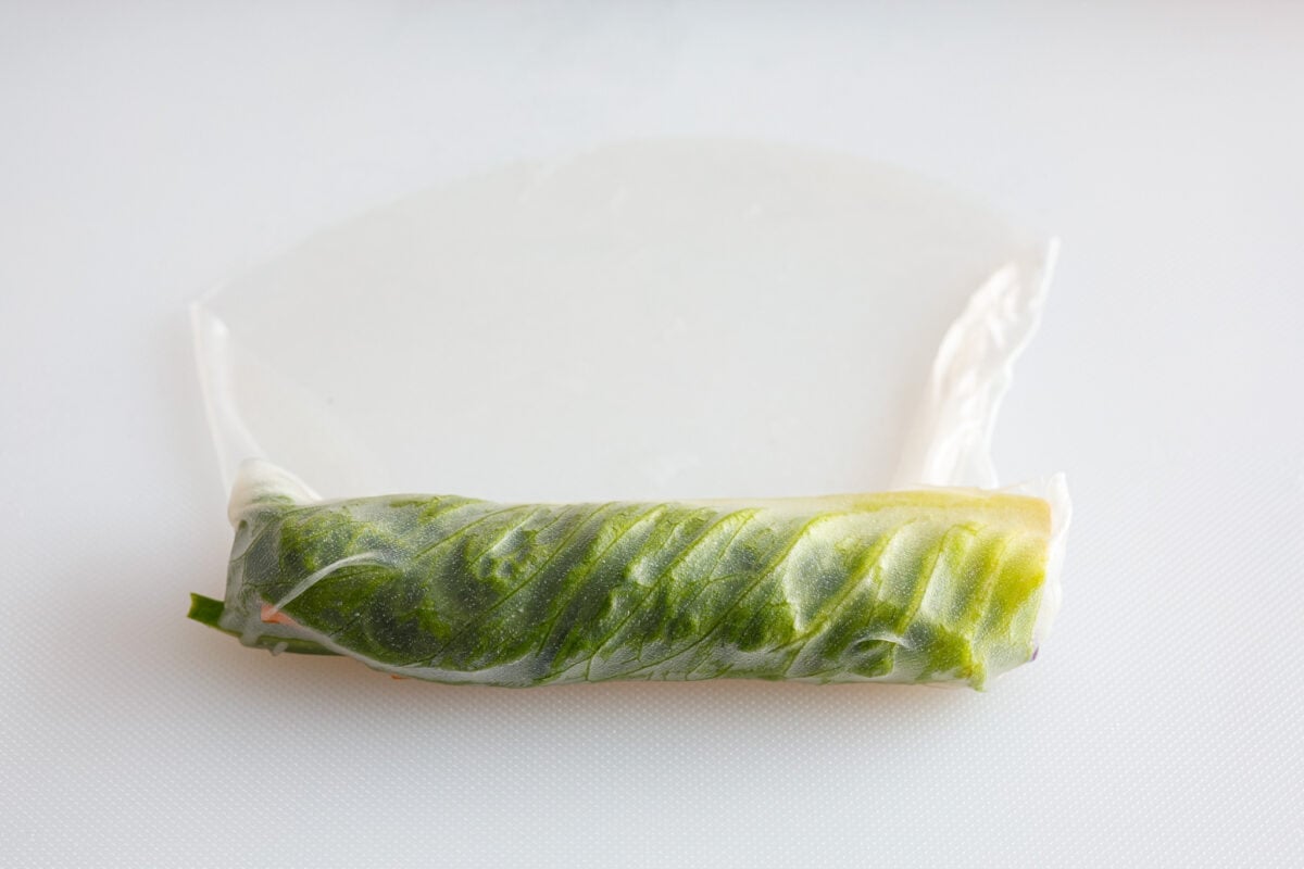 Spring rolls are a delightful, fresh, and vibrant snack that's perfect for any occasion. With ingredients like crisp carrots, refreshing mint, and tender rice vermicelli, these rolls are not only healthy but also bursting with flavor. A spring roll being rolled up.