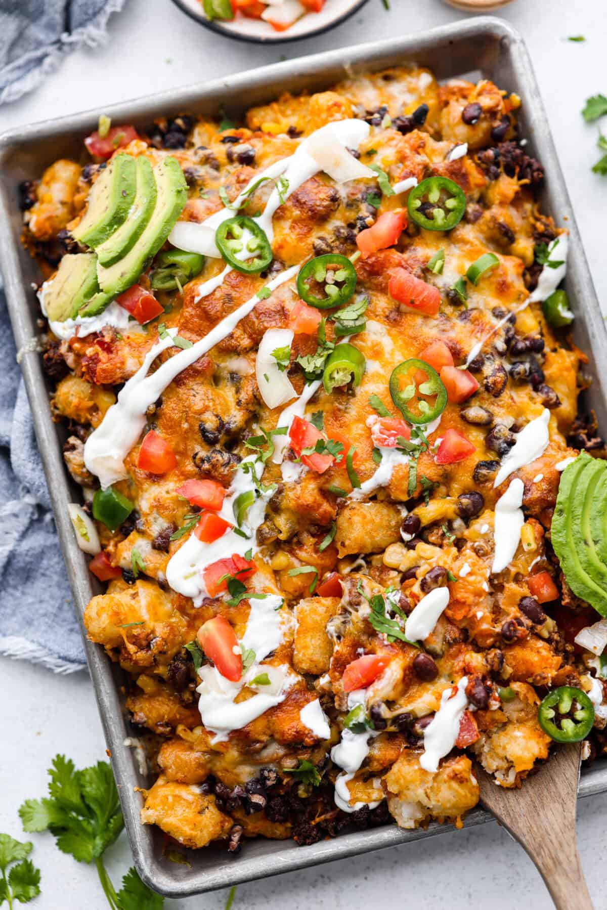 Tater Tot Nachos (Totchos) are made with crispy golden tater tots, topped with seasoned beef, scoops of refried beans, corn, black beans, salsa and melty cheese. Add your favorite toppings and dig in! Overhead shot of pan of tater tot nachos.