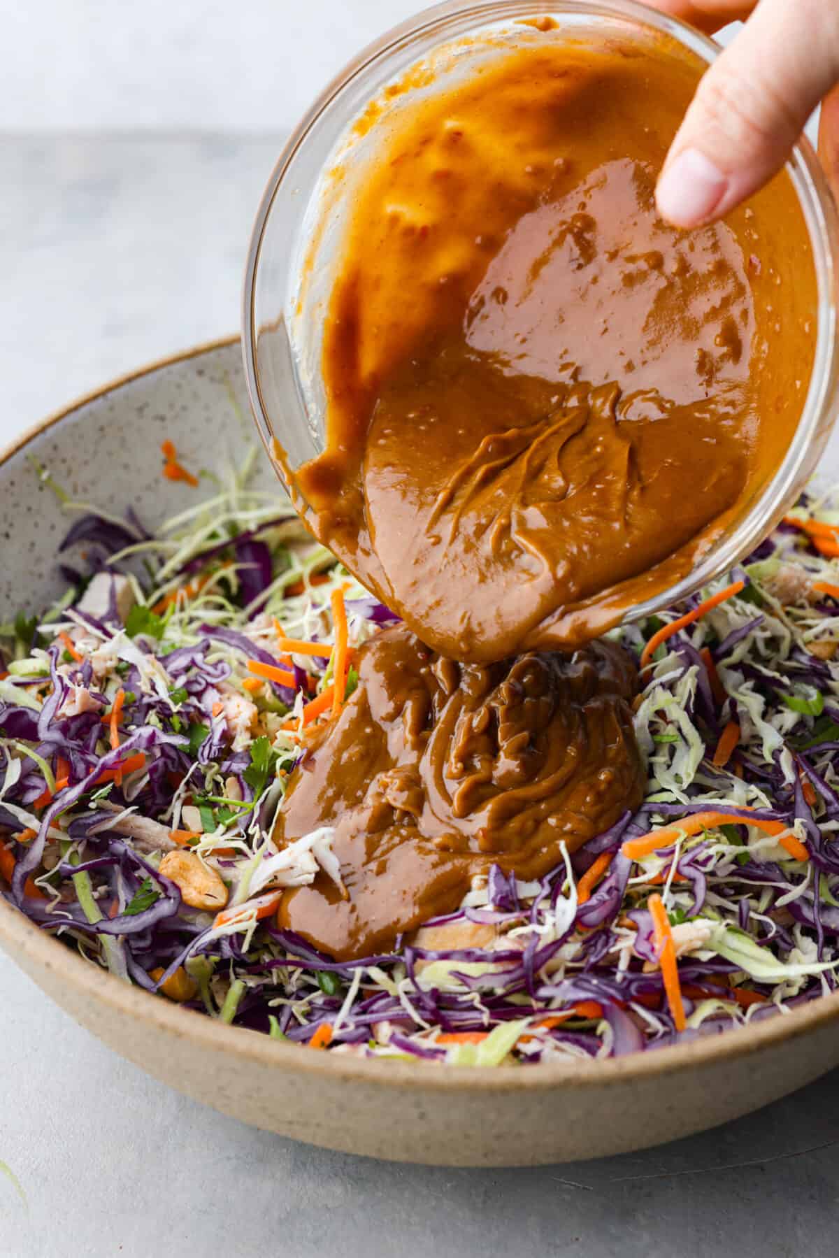 Crunchy and bright, this Thai Chicken Salad with creamy peanut dressing is bursting with flavor, texture and deliciousness! Prep it in under 30 minutes for an easy side dish or a delicious lunch! The salad dressing being added to the salad.