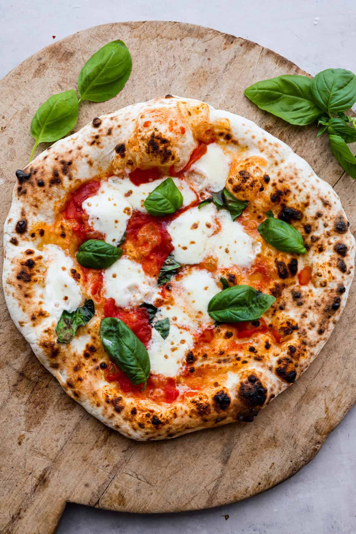 This is the perfect beginner's guide for making wood-fired pizza dough! Pizza expert, Chef Brandon Price, taught me how to make authentic homemade pizza, and now you get to learn too! Top view of wood-fired pizza on a wood cutting board.