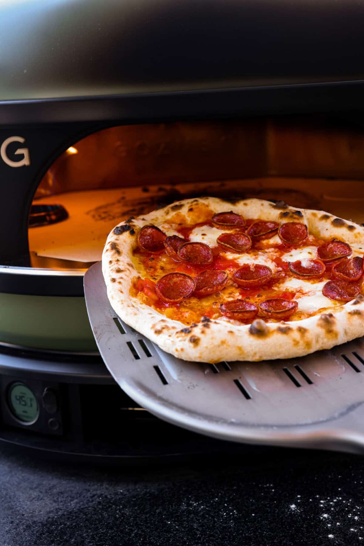 This is the perfect beginner's guide for making wood-fired pizza dough! Pizza expert, Chef Brandon Price, taught me how to make authentic homemade pizza, and now you get to learn too! Close view of a pizza spatula removing cooked wood-fired pizza from the oven.