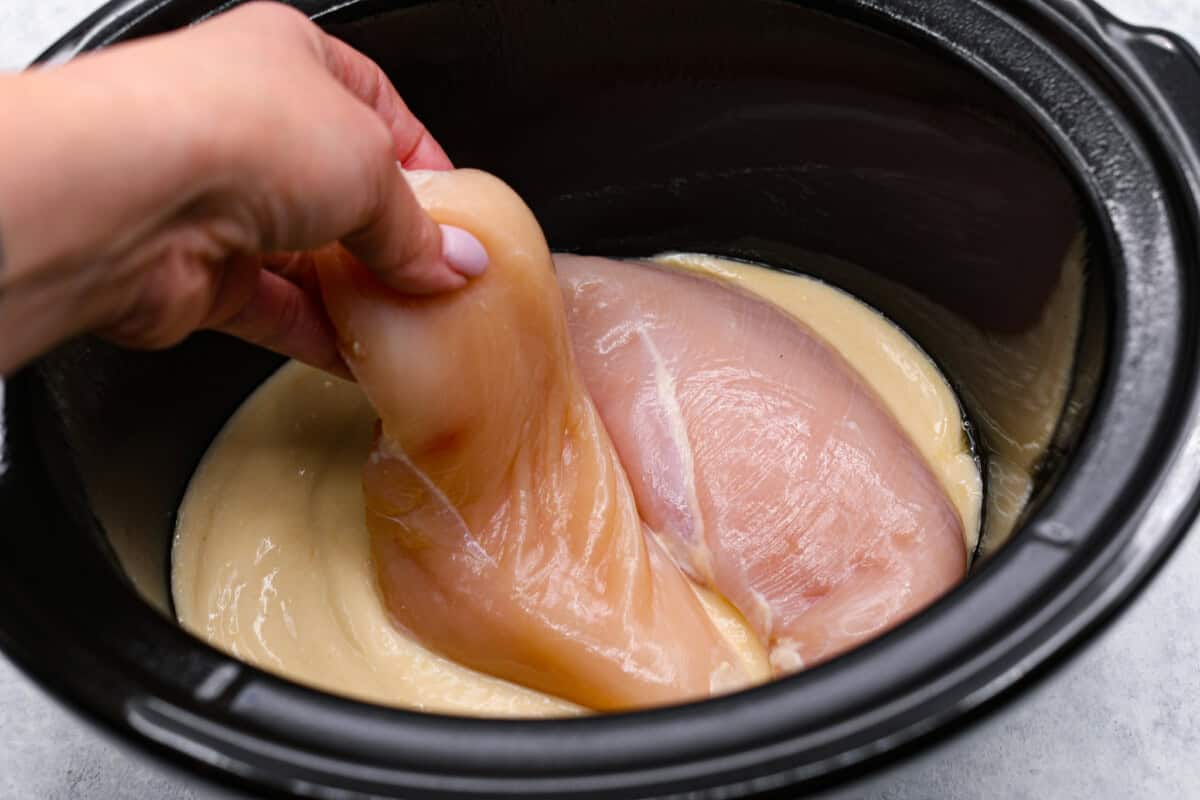 Treat yourself to this easy, Slow Cooker Chicken Cordon Bleu recipe! With tender chicken, savory ham, and melty Swiss cheese, it's a perfect comfort meal for any day. Chicken added to crockpot that has cream of chicken soup on the bottom.