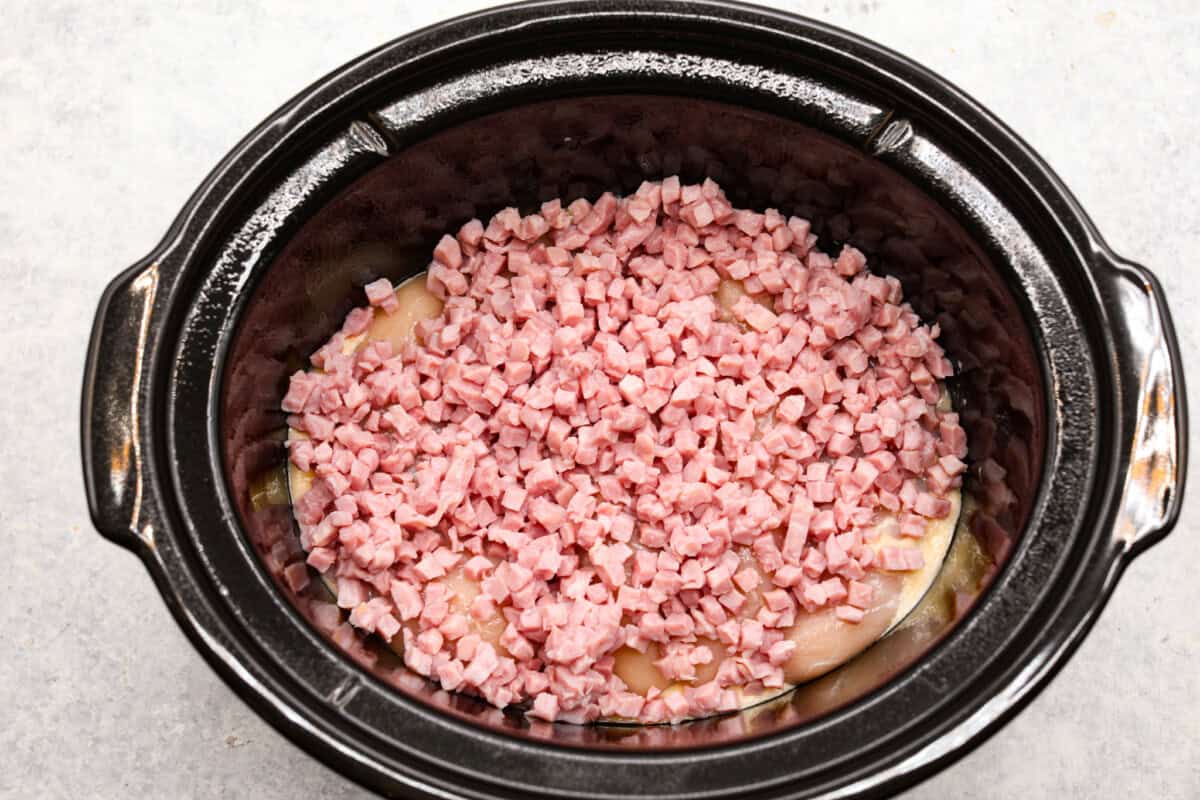 Treat yourself to this easy, Slow Cooker Chicken Cordon Bleu recipe! With tender chicken, savory ham, and melty Swiss cheese, it's a perfect comfort meal for any day. Ham being added to the crockpot.