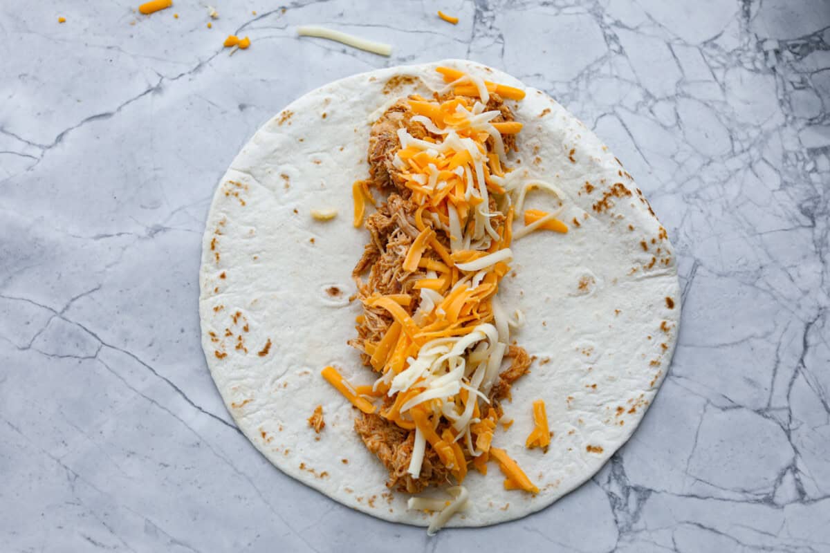Honey lime chicken enchiladas are a family favorite! These enchiladas are filled with shredded chicken and melty cheese and then smothered in a creamy enchilada sauce. The combination of honey and lime takes these enchiladas to the next level! Second photo of shredded chicken and cheese added to the tortillas.