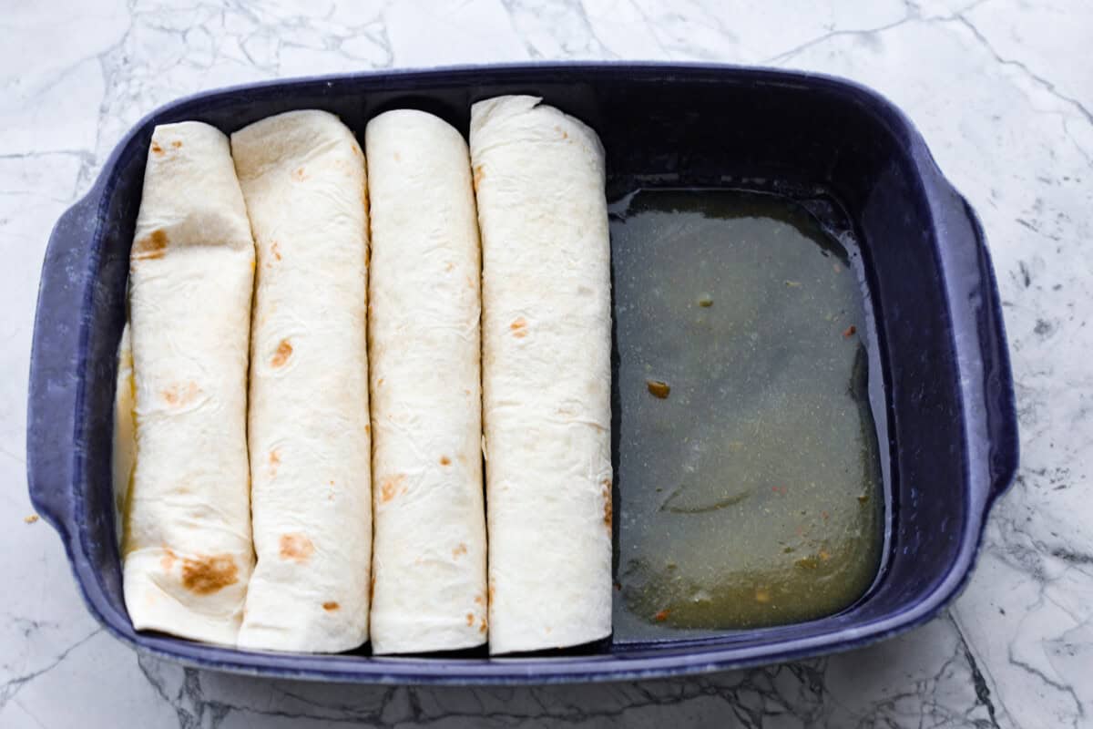 Honey lime chicken enchiladas are a family favorite! These enchiladas are filled with shredded chicken and melty cheese and then smothered in a creamy enchilada sauce. The combination of honey and lime takes these enchiladas to the next level! Third photo of the enchiladas rolled and placed into the baking dish.