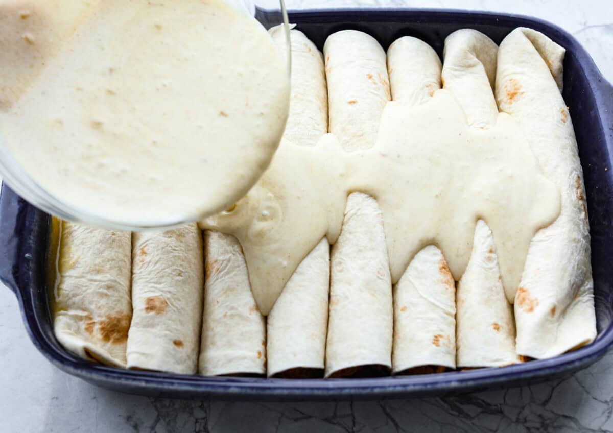 Honey lime chicken enchiladas are a family favorite! These enchiladas are filled with shredded chicken and melty cheese and then smothered in a creamy enchilada sauce. The combination of honey and lime takes these enchiladas to the next level! Fifth photo of the sauce pouring on the enchiladas.