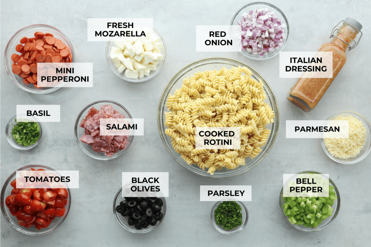 Indulge in the flavors of Italy with this irresistible Italian pasta salad! Each bite will be bursting with flavor from cherry tomatoes, creamy mozzarella, salami, olives, and fresh herbs topped with Italian dressing. Overhead shot of all of the ingredients in glass bowls and individually labeled.