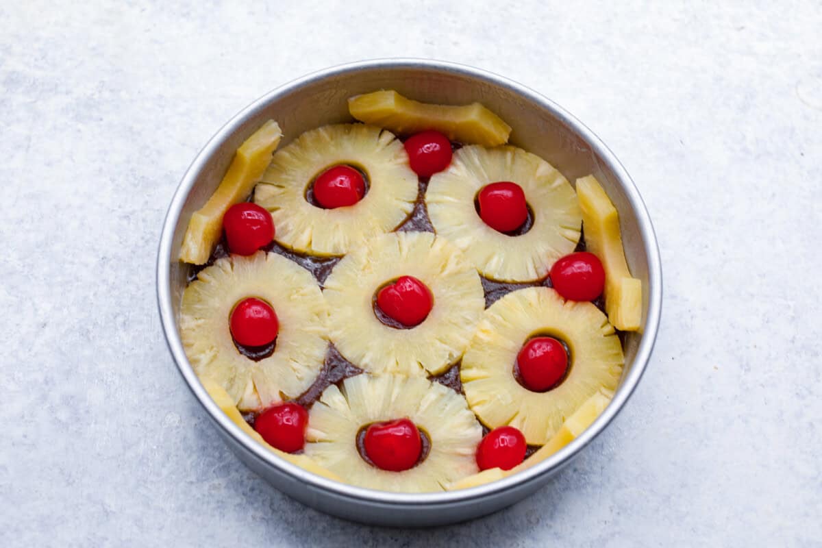 Perfect Pineapple Upside-Down Cake is a moist and fruity pineapple cake topped with caramelized pineapple rings and sweet maraschino cherries. It's no wonder this classic dessert has been a tried and true favorite for years! Fourth photo of the pineapple rings and cherries placed on the topping.