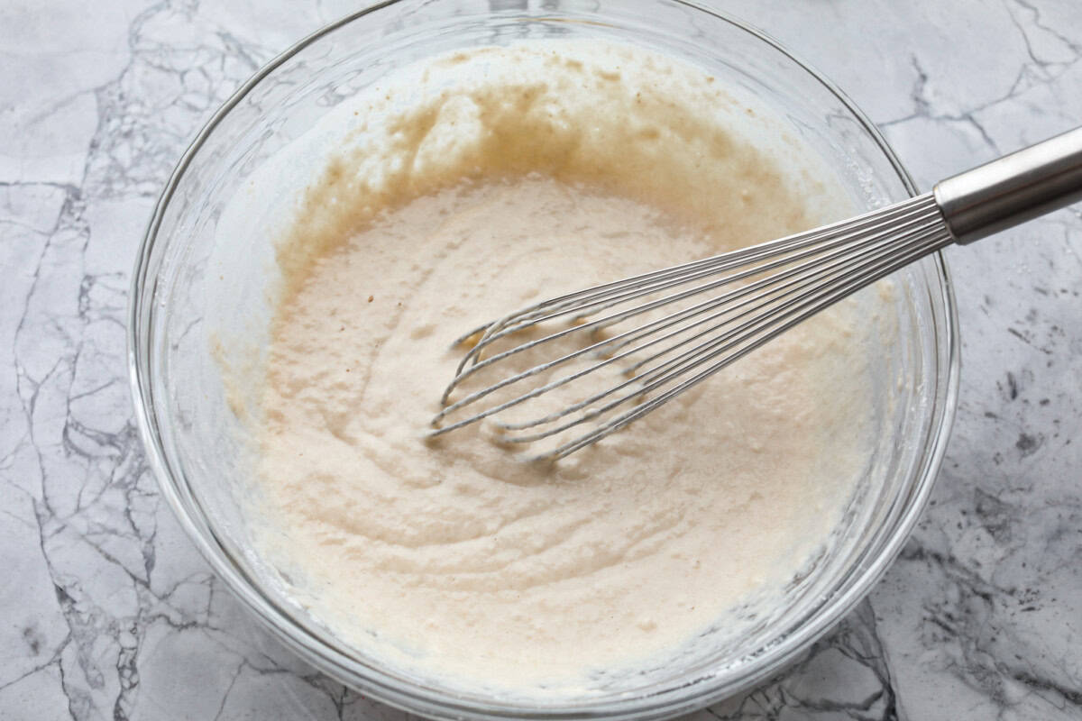 Whip up a batch of these delightful zeppole, perfect for a sweet treat anytime! With a light, fluffy texture and a generous coating of powdered or cinnamon sugar, these Italian donuts are sure to please. Overhead shot of wet and dry ingredients for zeppoles all mixed together in a bowl with a whisk.