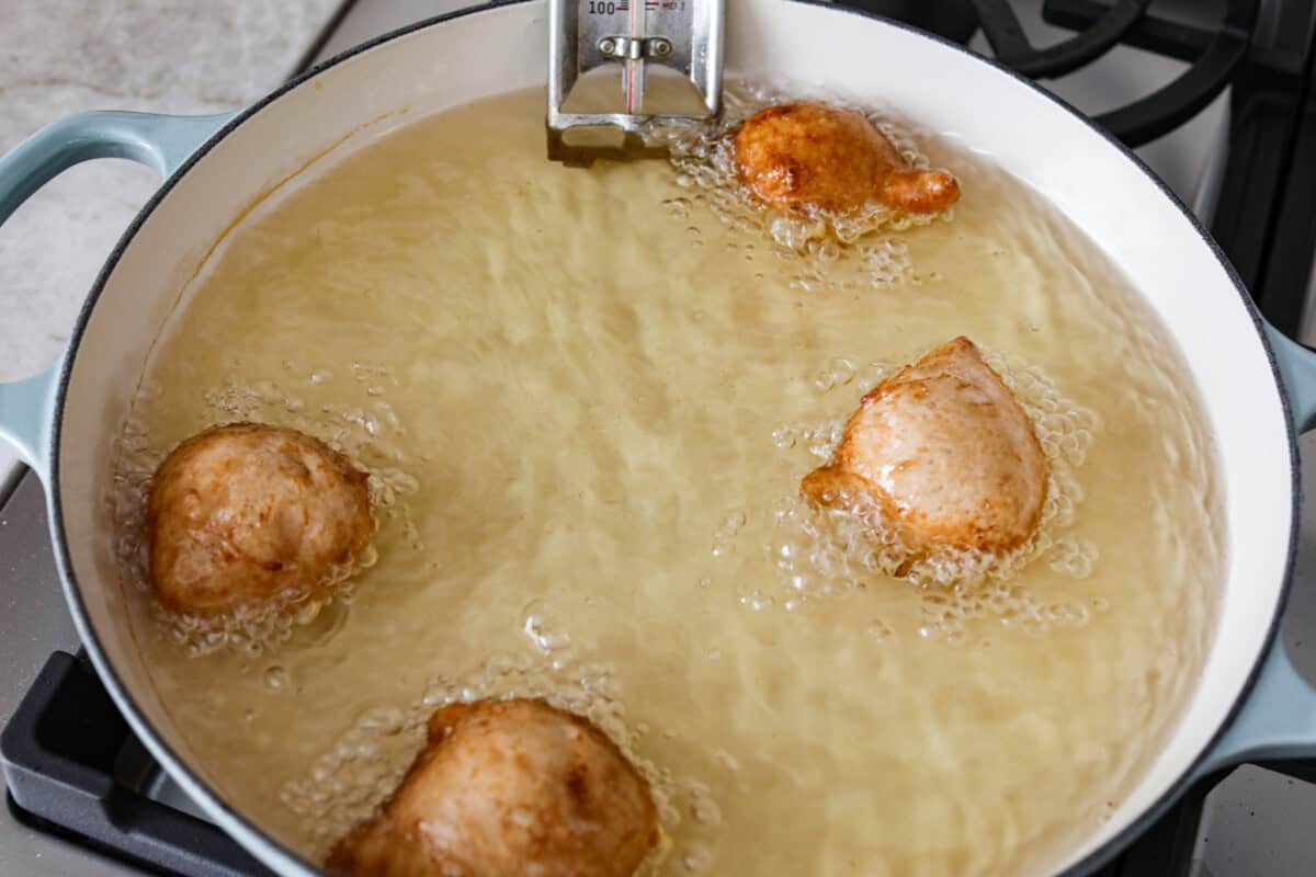 Whip up a batch of these delightful zeppole, perfect for a sweet treat anytime! With a light, fluffy texture and a generous coating of powdered or cinnamon sugar, these Italian donuts are sure to please. overhead shot of zeppole being fried in oil.
