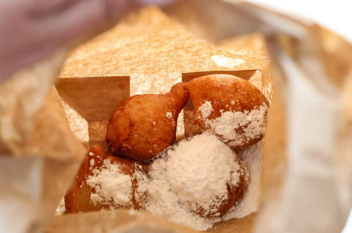 Whip up a batch of these delightful zeppole, perfect for a sweet treat anytime! With a light, fluffy texture and a generous coating of powdered or cinnamon sugar, these Italian donuts are sure to please. close up shot of zeppoles in paper bag with powdered sugar.