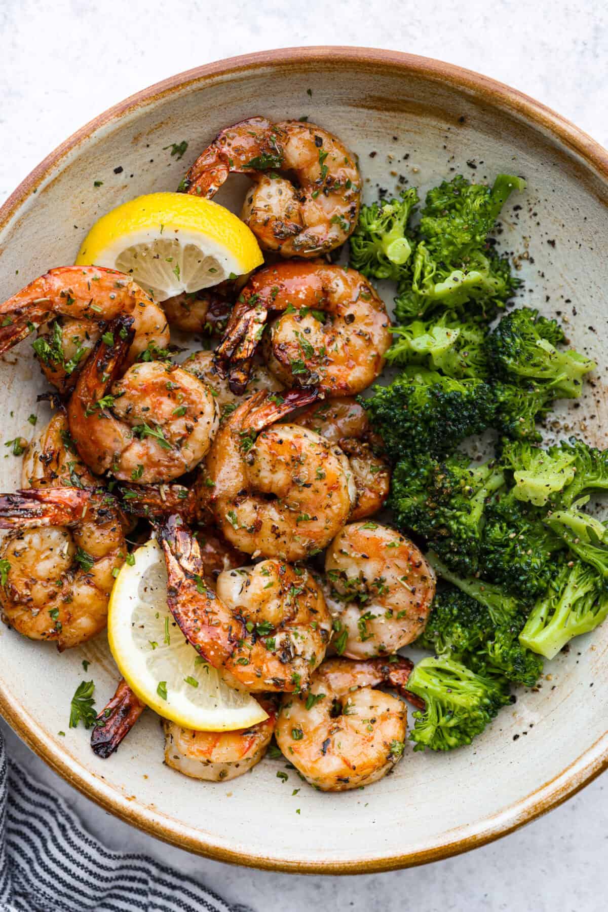 This air fryer shrimp is tender, delicious, and so easy to make! With only a few ingredients, the marinated shrimp cooks to perfection and has the best flavor! Top view of air fryer shrimp in a bowl with broccoli and garnished with lemon.