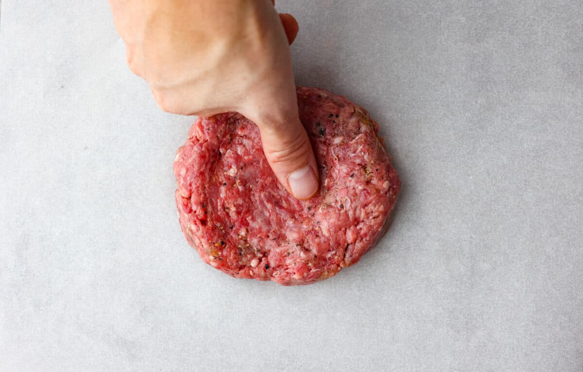 Get ready for the ultimate burger experience topped with my irresistible Secret Sauce. The flavor packed into this burger is a delicious twist on a classic favorite. Someone indenting the ground beef with their thumb.