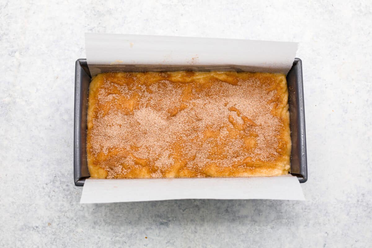 Cinnamon Swirl Banana Bread is a delightful twist on the classic. What sets this recipe apart is the luscious cinnamon sugar swirl running through the middle and on top, creating a beautiful marbled effect and an extra burst of flavor. It's irresistibly delicious! Overhead shot of batter in bread pan covered in cinnamon and sugar.