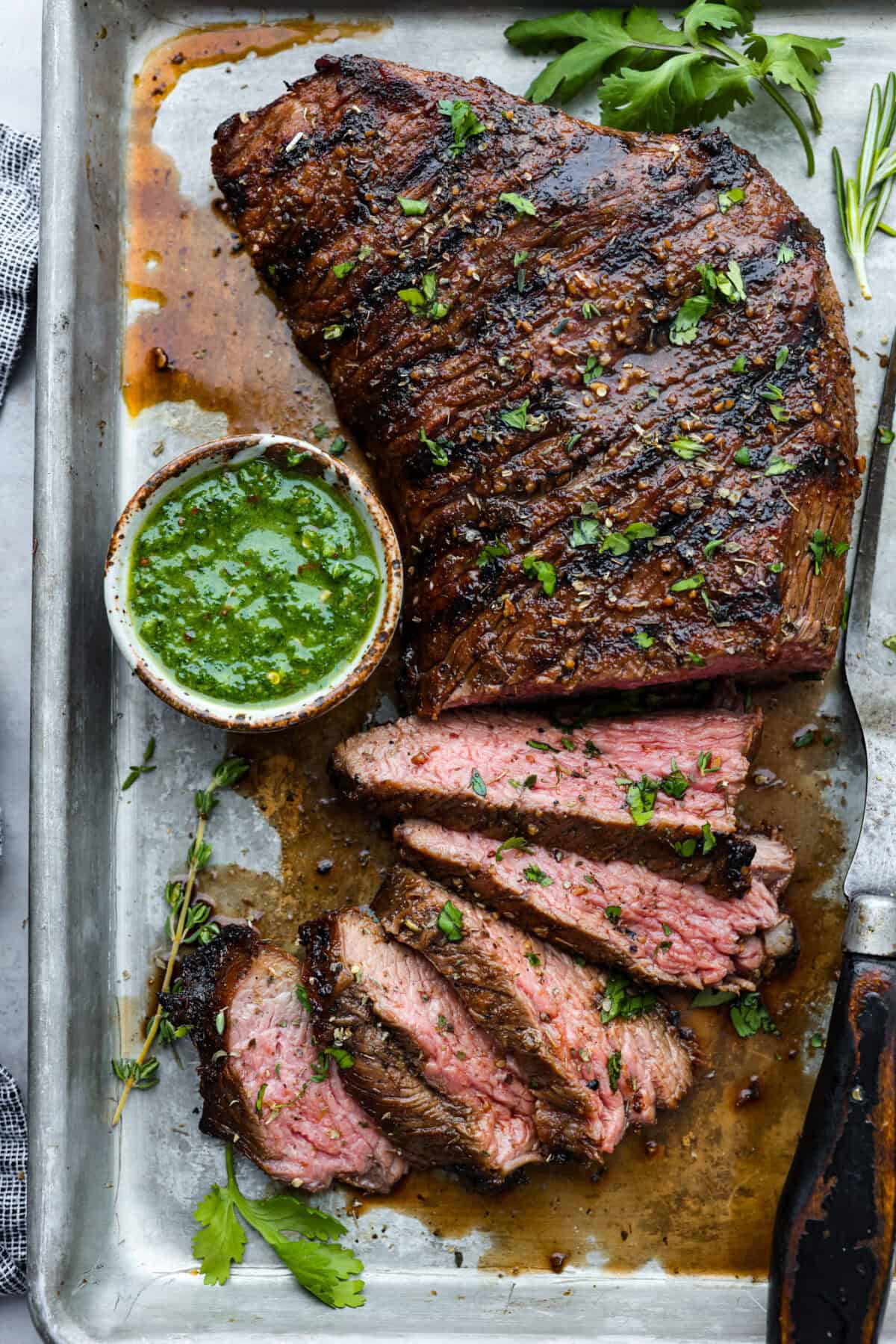 Grilled Tri-Tip is a flavorful, juicy steak that will be the star of your barbecue! It's marinated in a simple, yet tasty marinade, then grilled to perfection. Serve with my sweet and savory chimichurri sauce and your favorite sides for an impressive meal that everyone will love! Overhead shot of grilled tri-tip that has a few slices taken off and a small bowl of chimichuri sauce next to it.