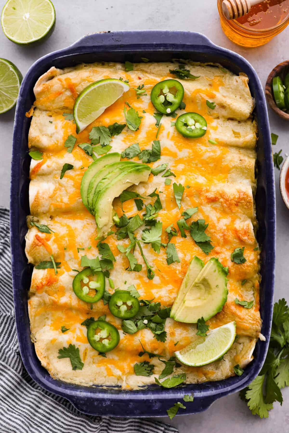 Honey lime chicken enchiladas are a family favorite! These enchiladas are filled with shredded chicken and melty cheese and then smothered in a creamy enchilada sauce. The combination of honey and lime takes these enchiladas to the next level! Top view of honey lime chicken enchiladas in a baking dish.