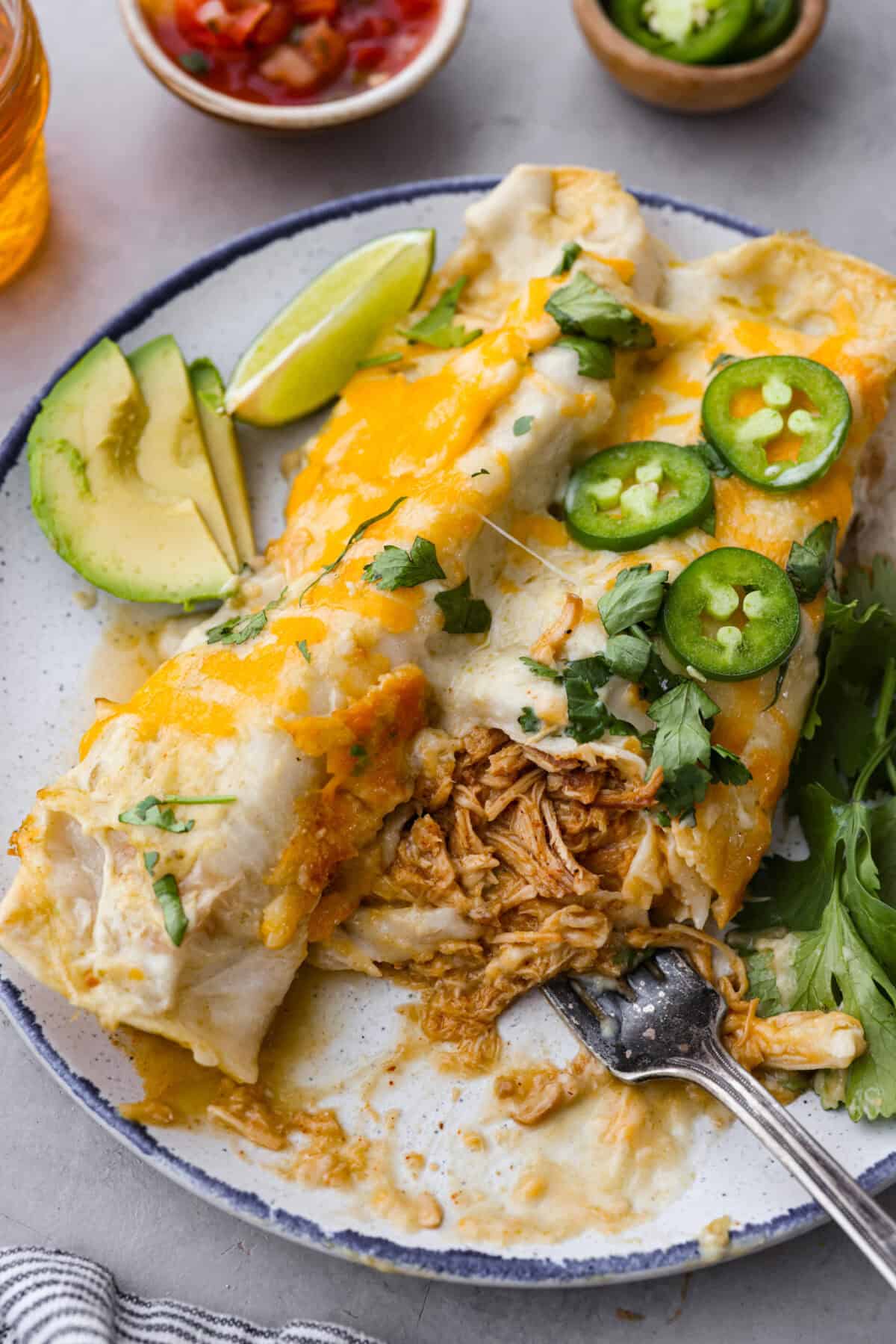 Honey lime chicken enchiladas are a family favorite! These enchiladas are filled with shredded chicken and melty cheese and then smothered in a creamy enchilada sauce. The combination of honey and lime takes these enchiladas to the next level! Close view of honey lime chicken enchiladas plated with a fork.
