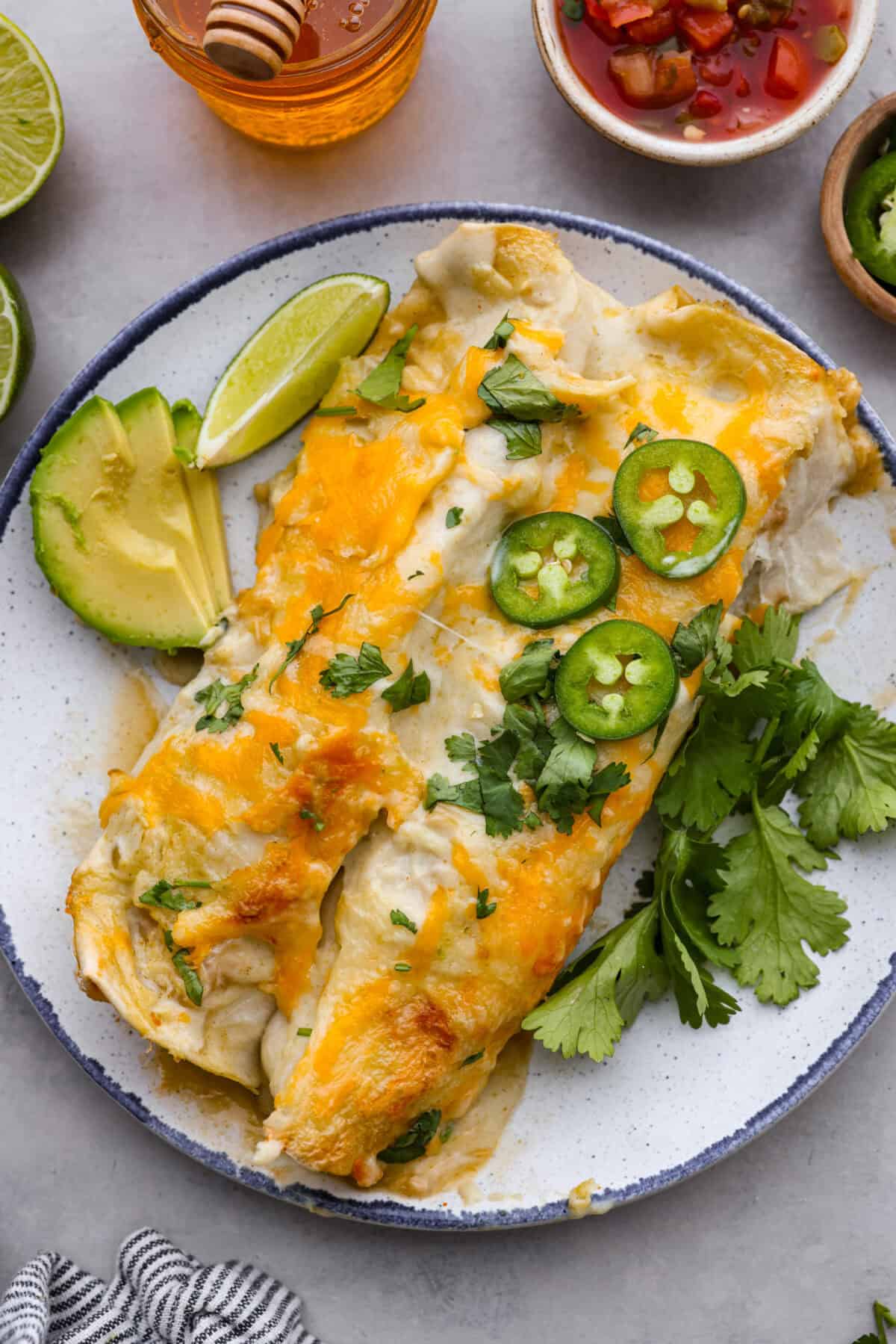 Honey lime chicken enchiladas are a family favorite! These enchiladas are filled with shredded chicken and melty cheese and then smothered in a creamy enchilada sauce. The combination of honey and lime takes these enchiladas to the next level! Close top view of honey lime chicken enchiladas plated and garnished.