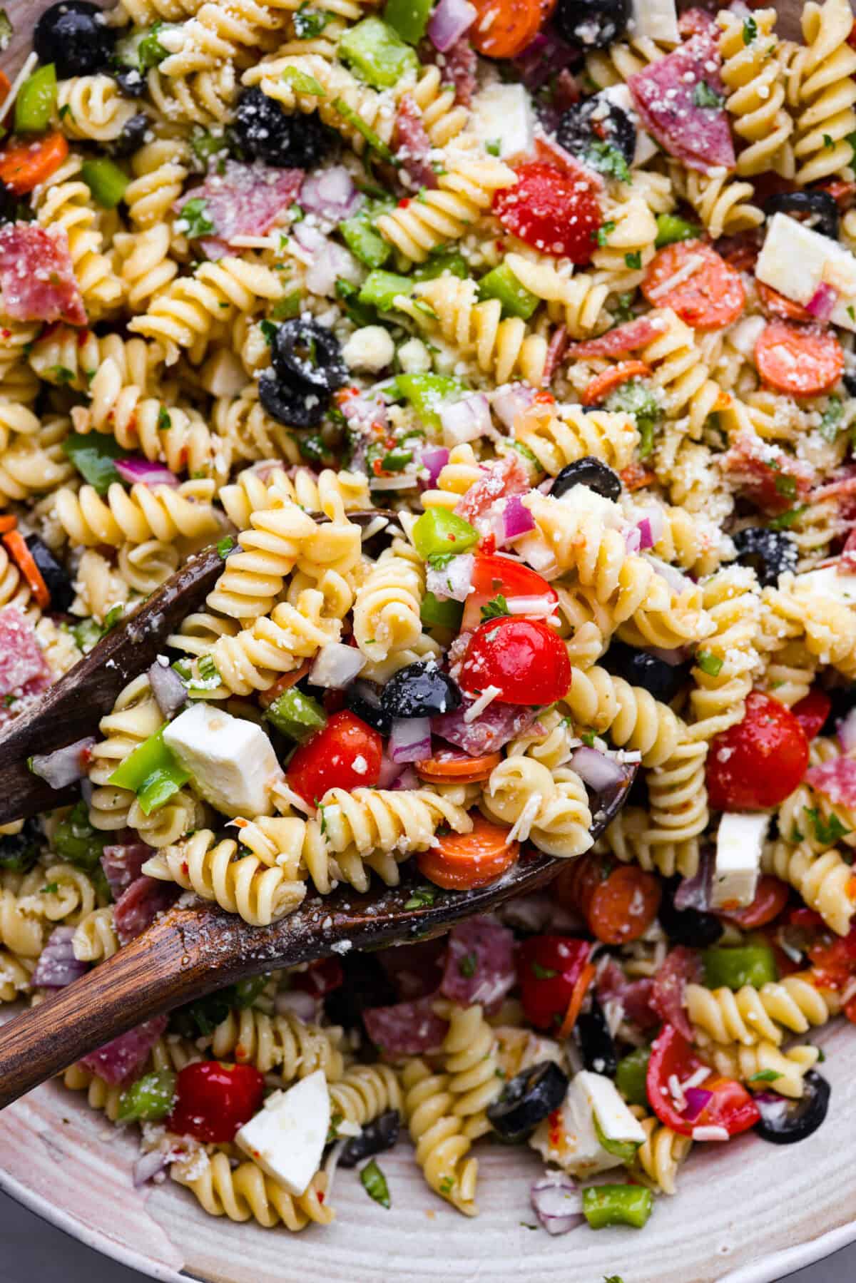 Indulge in the flavors of Italy with this irresistible Italian pasta salad! Each bite will be bursting with flavor from cherry tomatoes, creamy mozzarella, salami, olives, and fresh herbs topped with Italian dressing. It's like a taste of sunny Italy! Close up shot of pasta salad with rotini noodles, tomatoes, bits of red onion, olives, salami, green pepper and cheese.