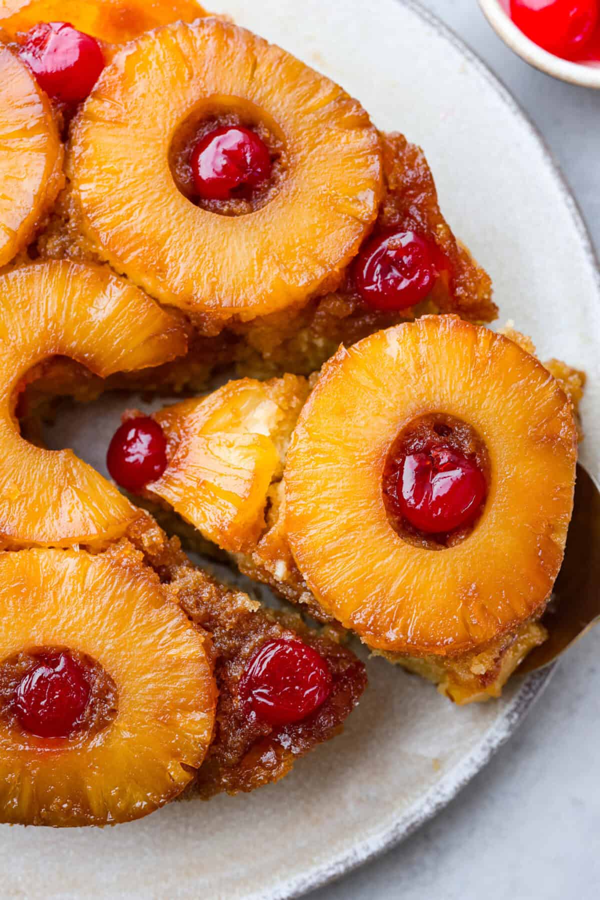 Perfect Pineapple Upside-Down Cake is a moist and fruity pineapple cake topped with caramelized pineapple rings and sweet maraschino cherries. It's no wonder this classic dessert has been a tried and true favorite for years! Close view of pineapple upside down cake with a slice lifting out.