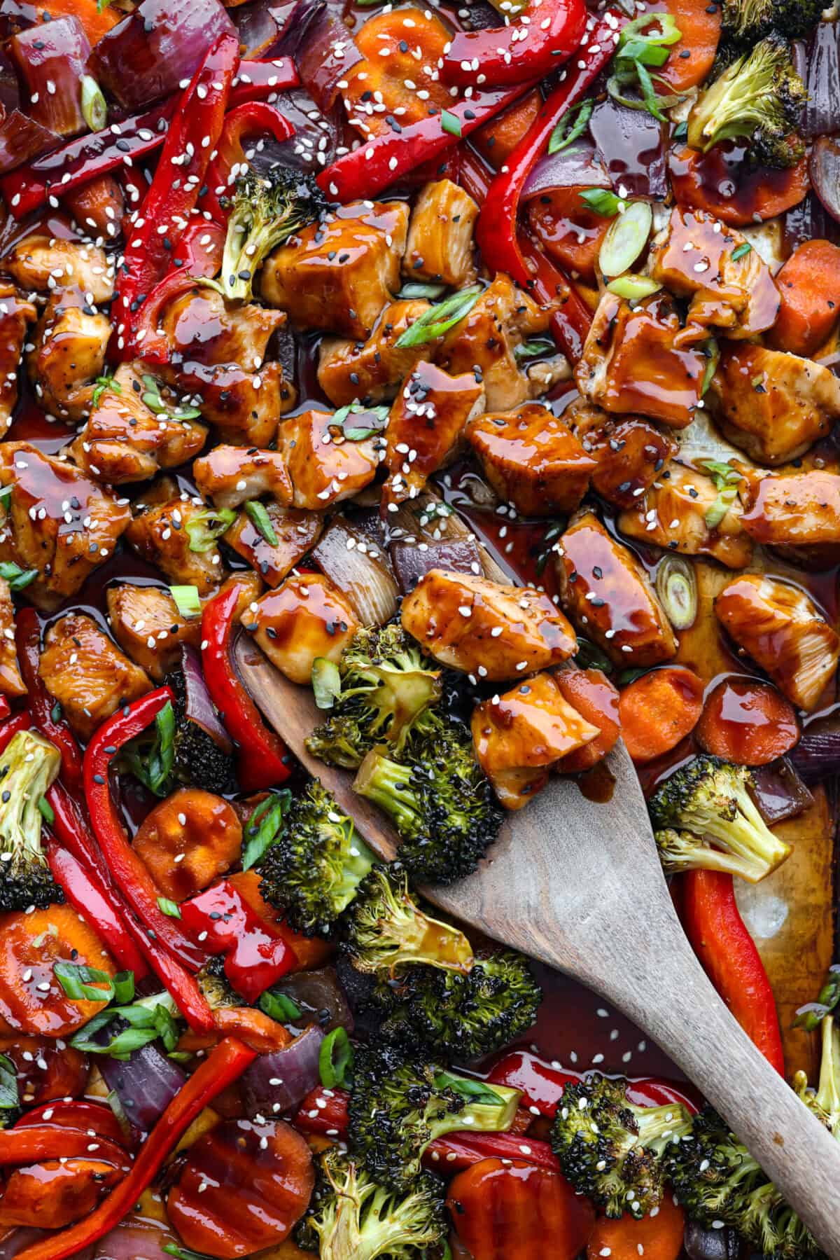 This sheet pan teriyaki chicken with vegetables is a family favorite! It's loaded with tender chicken and veggies that get tossed in a homemade teriyaki sauce. A one pan dinner recipe that is super easy to throw together. Close view of sheet pan teriyaki chicken with vegetables with a wood spatula.