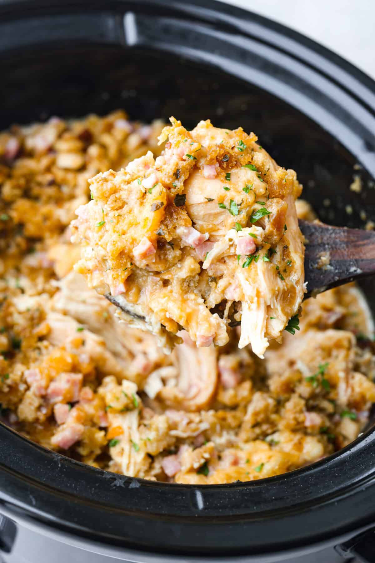 Treat yourself to this easy, Slow Cooker Chicken Cordon Bleu recipe! With tender chicken, savory ham, and melty Swiss cheese, it's a perfect comfort meal for any day. A close up of scooped chicken cordon bleu from a crockpot with a wooden spoon.
