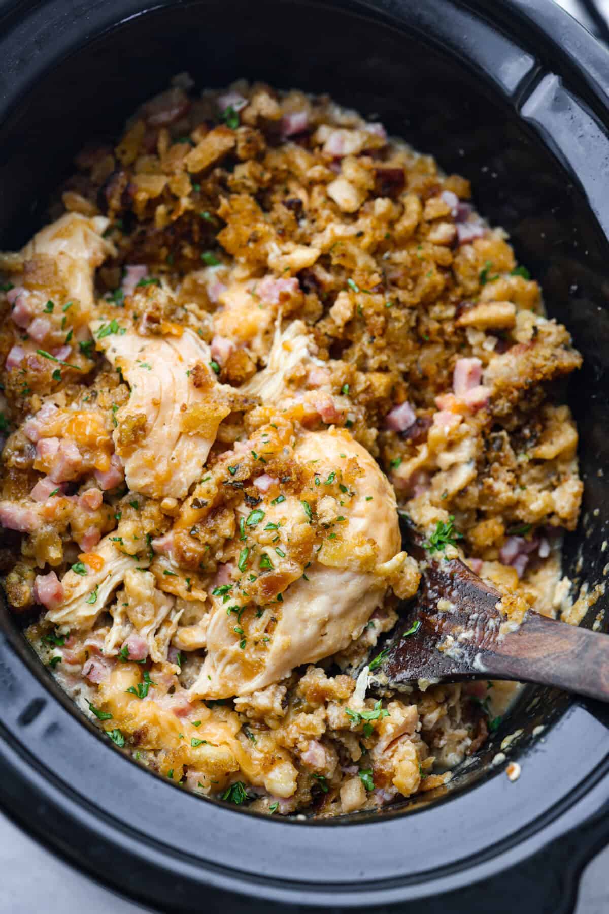 Treat yourself to this easy, Slow Cooker Chicken Cordon Bleu recipe! With tender chicken, savory ham, and melty Swiss cheese, it's a perfect comfort meal for any day. Slow cooker chicken cordon bleu in the crockpot being scooped out with a wooden spoon.